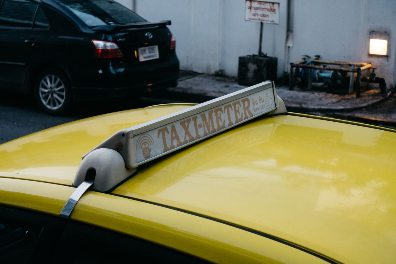 Close-up of a yellow taxi's roof with a taxi meter sign in an urban environment.